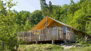 Tenda safari con terrazza in legno e recinzione, immersa tra alberi verdi in un paesaggio boscoso.