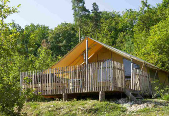 Safari-Zelt mit Holzterrasse im grünen Wald, umgeben von Bäumen, perfekt für naturnahen Urlaub.