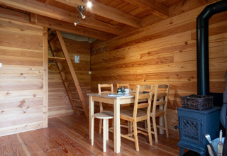Interior de tienda safari Cahutte con paredes de madera, mesa, sillas, estufa y escalera al altillo.