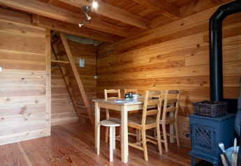 Interior de tienda safari Cahutte con paredes de madera, mesa, sillas, estufa y escalera al altillo.