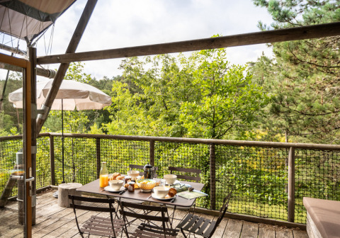Outdoor terrace of a Cahutte safari tent set for breakfast with a view of lush green forest trees.