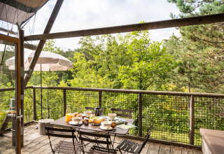Terraza al aire libre de una tienda Cahutte con desayuno servido y vistas al bosque verde y frondoso.