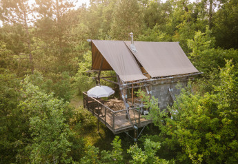Cahutte safaritent met verhoogd terras, parasol en zitplaatsen midden in het groene bosrijke landschap.