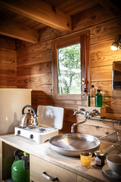 Acogedora cocina en una tienda safari Cahutte con estufa de gas, hervidor, fregadero y paredes de madera.