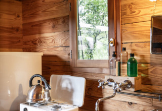 Acogedora cocina en una tienda safari Cahutte con estufa de gas, hervidor, fregadero y paredes de madera.