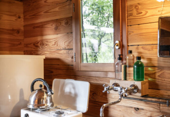 Coin cuisine chaleureux d'une tente safari Cahutte avec réchaud à gaz, bouilloire, évier et murs boisés.