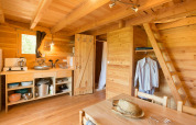 Acogedor interior de la tienda safari Cahutte, con paredes de madera, cocina sencilla y una escalera.