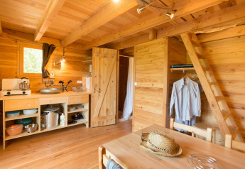 Acogedor interior de la tienda safari Cahutte, con paredes de madera, cocina sencilla y una escalera.
