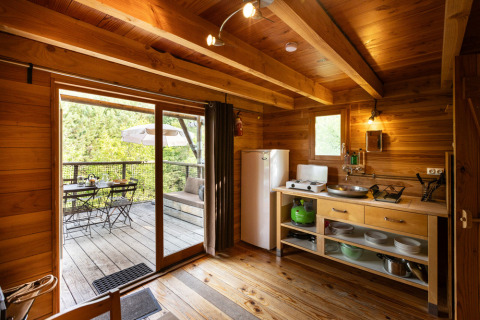 Interior of the Cahutte safari tent with wooden kitchen, dining area, and view of outdoor terrace seating.