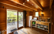Interno della tenda safari Cahutte con cucina in legno, tavolo e vista sulla terrazza arredata all'aperto.