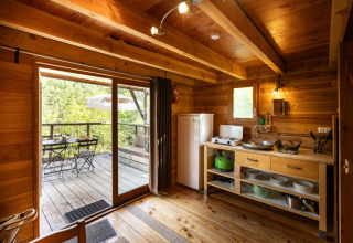 Interieur van de safari-tent Cahutte met houten keuken, eethoek en uitzicht op gemeubileerd terras.