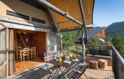 Terraza exterior en una tienda safari Cahutte con comedor, sofá y vistas a colinas boscosas.