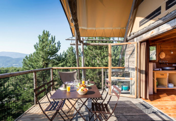 Terrasse eines Cahutte Safari-Zeltes mit Holzmöbeln, Frühstück und Blick auf Wald und Berge.