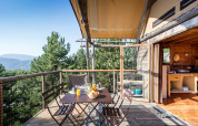 Terraza exterior en una tienda Cahutte con mesa de desayuno, rodeada de bosque y vistas a la montaña.