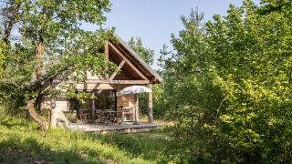 Accogliente baita in legno con veranda e ombrellone, immersa in una rigogliosa vegetazione boschiva.