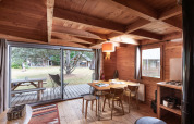 Acogedora cabaña con comedor de madera, grandes ventanas a una terraza y vista al jardín al aire libre.