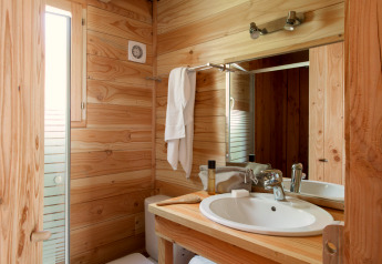 Salle de bain de cabine chaleureuse avec murs en bois, vasque blanche, miroir et fenêtre lumineuse.