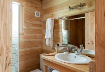 Knusse badkamer in een houten chalet met houten muren, een witte lavabo, spiegel en raam met daglicht.