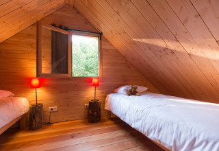 Et hyggeligt loftsværelse i en hytte med to enkeltsenge, træpaneler og rød belysning fra lamper.