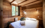 Acogedor dormitorio en una cabaña de madera con cama doble, ventana abierta y bolsas sobre la cama.