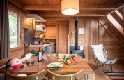 Interno di cabina accogliente con tavolo da pranzo, verdure fresche, vino, cucina e stufa a legna.