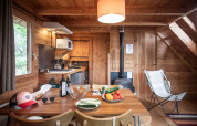 Gezellige houten chalet met tafel vol groenten, wijn, keuken en houtkachel in de achtergrond zichtbaar.