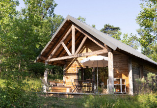Een gezellige houten chalet omringd door groene natuur en bomen, badend in zonlicht op een rustige dag in de natuur.