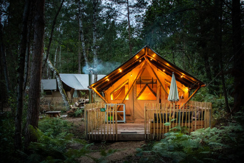 Tienda safari iluminada Tente Trappeur Duo Village en Village Huttopia Lac de Rillé, Francia, en el bosque.