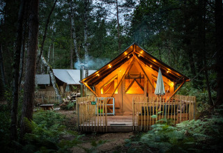 Tienda safari iluminada Tente Trappeur Duo Village en Village Huttopia Lac de Rillé, Francia, en el bosque.