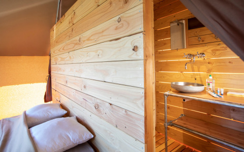 Vista interna della Tente Trappeur Duo Village a Huttopia Lac de Rillé, con letto e bagno in legno.