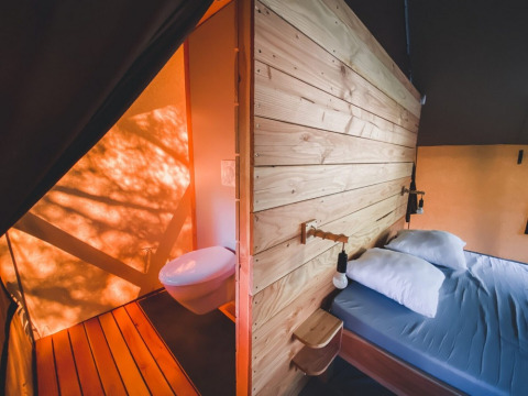 Innenansicht eines Safari-Zeltes mit Doppelbett und Badezimmer im Tente Trappeur Duo Village, Huttopia Lac de Rillé, Frankreich.