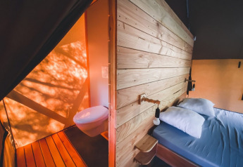 Interno di tenda safari con letto matrimoniale e bagno presso Tente Trappeur Duo Village, Huttopia Lac de Rillé, Francia.