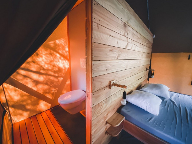 Innenansicht eines Safari-Zeltes mit Doppelbett und Badezimmer im Tente Trappeur Duo Village, Huttopia Lac de Rillé, Frankreich.