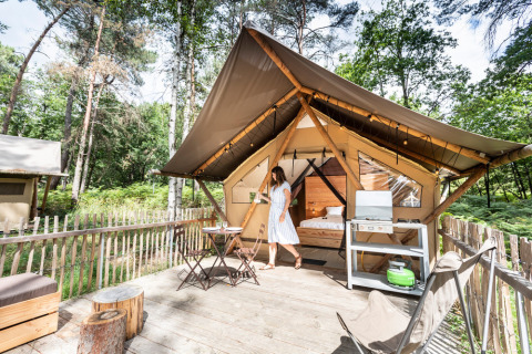 Kvinde foran en luksuriøs safari-telt ved Village Huttopia Lac de Rillé med terrasse og skovudsigt.
