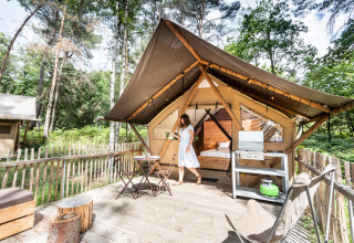 Kvinde foran en luksuriøs safari-telt ved Village Huttopia Lac de Rillé med terrasse og skovudsigt.