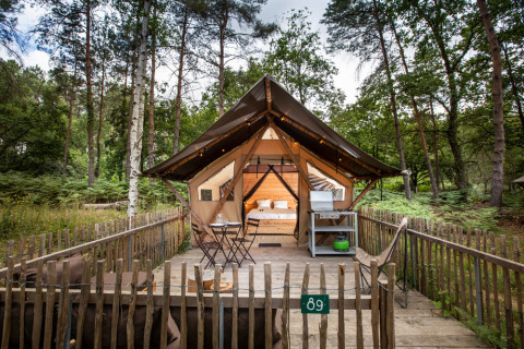 Tienda safari Tente Trappeur Duo Village con terraza de madera en el bosque de Huttopia Lac de Rillé, Francia.