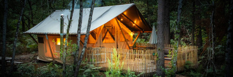 Tienda safari Tente Trappeur Duo Village en Village Huttopia Lac de Rillé, Francia, iluminada en el bosque.