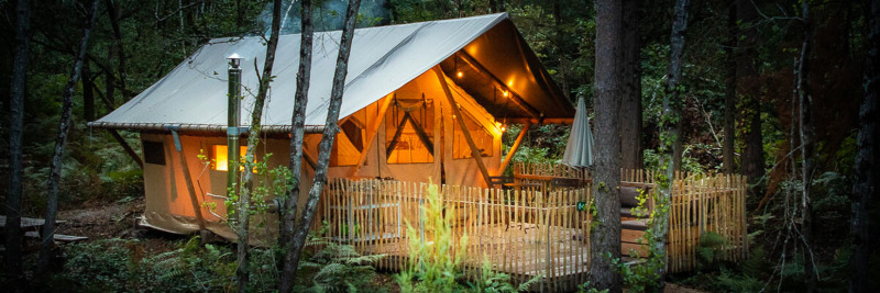 Safari tent Tente Trappeur Duo Village at Village Huttopia Lac de Rillé, France, warmly lit in the forest.