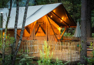 Tente safari Tente Trappeur Duo Village au Village Huttopia Lac de Rillé, France, éclairée en pleine forêt.