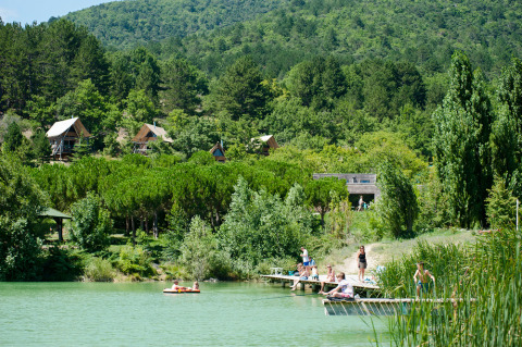 Personas disfrutando en el lago y cabañas en el bosque en Village Huttopia Dieulefit, Auvergne-Rhône-Alpes, Francia.