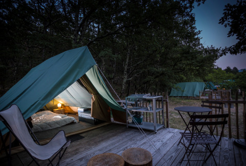 Tienda glamping iluminada con terraza y muebles exteriores en Village Huttopia Dieulefit, Auvergne-Rhône-Alpes.