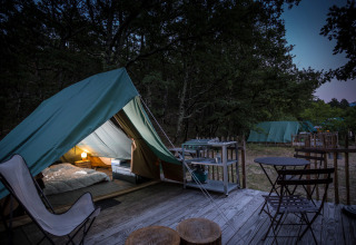 Sfeervolle glampingtent met houten terras en zitruimte bij Village Huttopia Dieulefit in Auvergne-Rhône-Alpes.