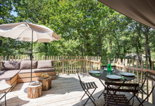 Houten terras in Huttopia Dieulefit met loungehoek, parasol, eettafel en zicht op groene natuur.