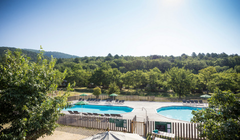 View of swimming pools and loungers surrounded by greenery at Village Huttopia Dieulefit holiday park, France.