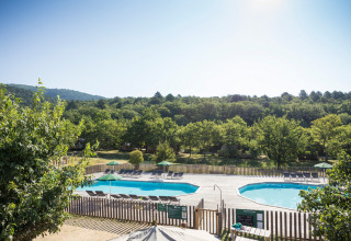 View of swimming pools and loungers surrounded by greenery at Village Huttopia Dieulefit holiday park, France.
