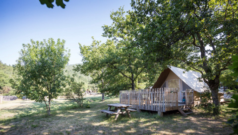 Tienda de campaña con terraza de madera bajo árboles en Village Huttopia Dieulefit, Auvergne-Rhône-Alpes, Francia.