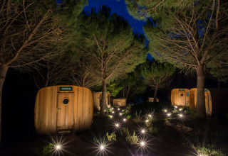 Night view at Huttopia Dieulefit holiday park with illuminated wooden cabins and trees in Auvergne-Rhône-Alpes, France.