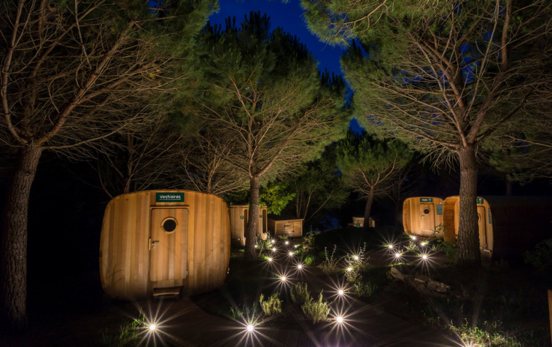 Nachtzicht op Huttopia Dieulefit met verlichte houten hutten tussen bomen in Auvergne-Rhône-Alpes, Frankrijk.
