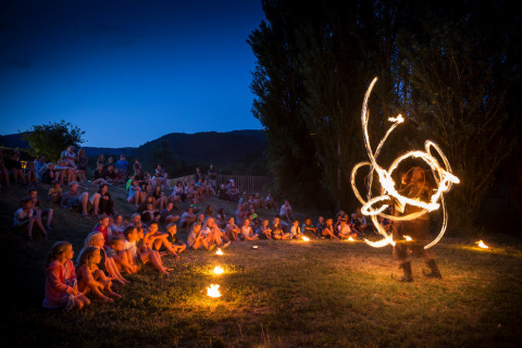 Niños en Village Huttopia Dieulefit observan un espectáculo de fuego al aire libre al anochecer en Francia.