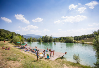 Ferienpark am See im Village Huttopia Dieulefit, Auvergne-Rhône-Alpes, Frankreich, mit sonnenbadenden Menschen.